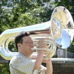 Musiker spielt im Freien ein großes glänzendes Blechblasinstrument